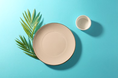 Ceramic plate, bowl and green leaves on turquoise background, flat lay