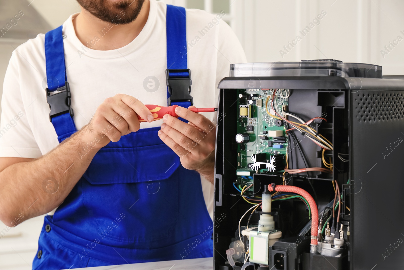 Photo of Repairman with screwdriver fixing coffee machine indoors, closeup