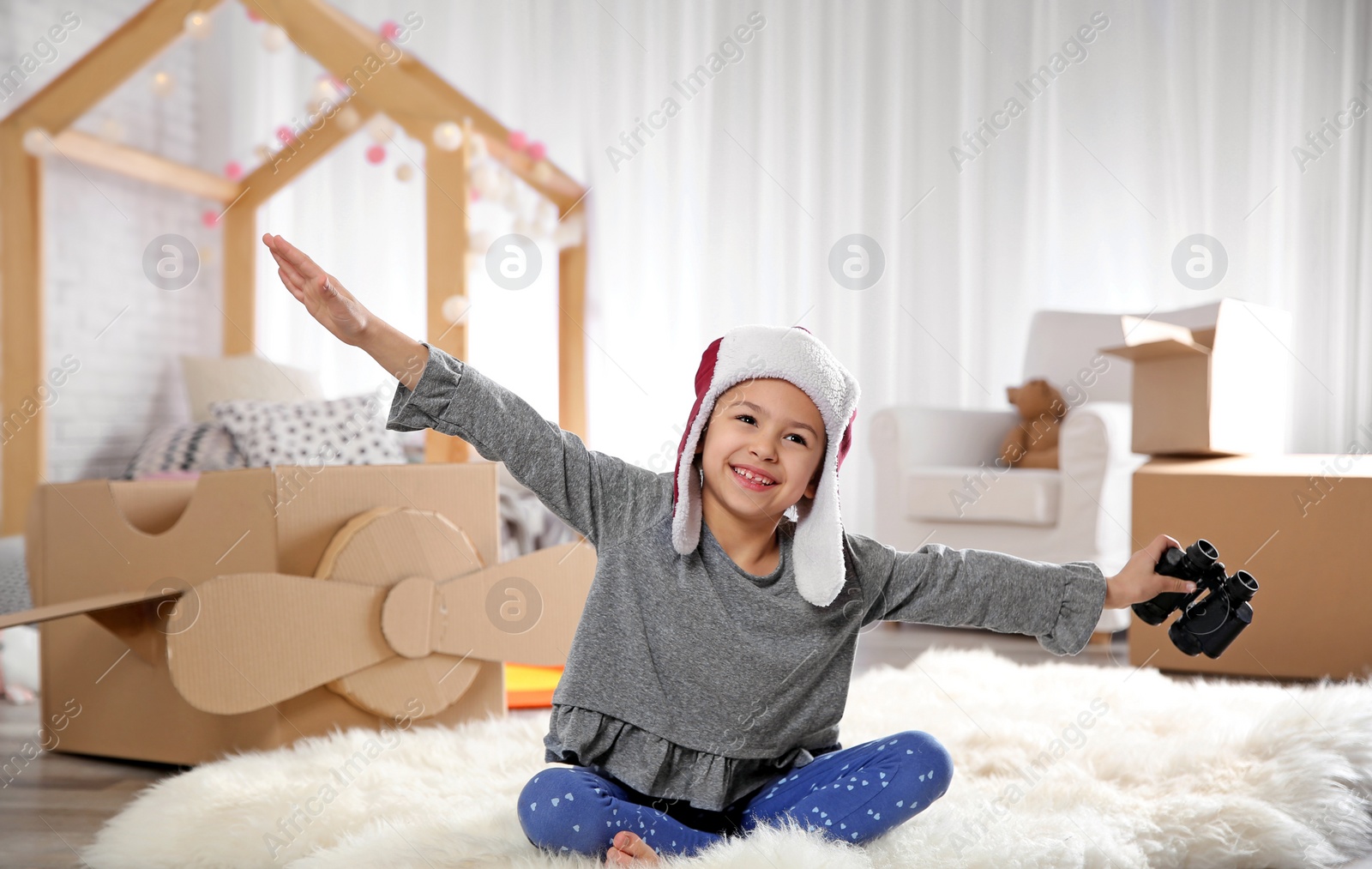 Photo of Cute little girl playing with binoculars and cardboard airplane in bedroom