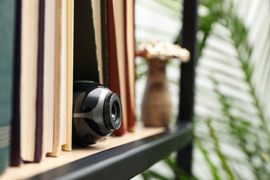 Photo of Camera hidden between books on wooden shelf indoors, closeup. Space for text