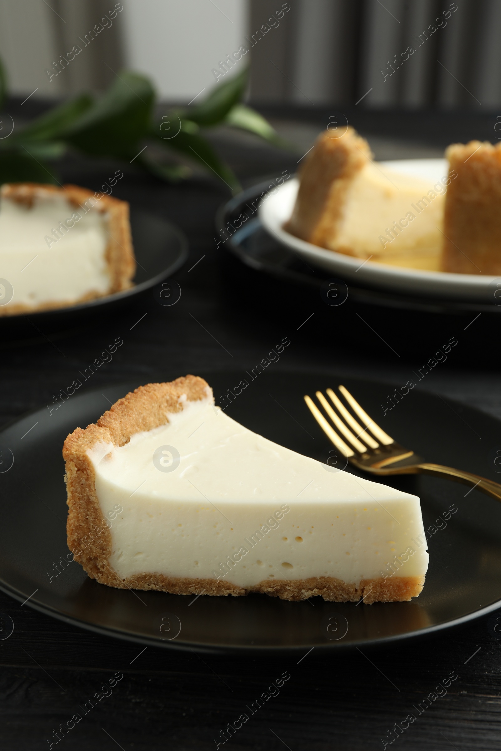 Photo of Piece of tasty vegan tofu cheesecake and fork on black wooden table, space for text