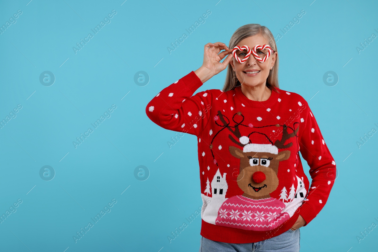 Photo of Senior woman in Christmas sweater and funny glasses on light blue background. Space for text