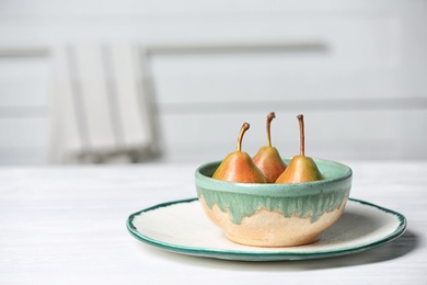 Photo of Dishware with pears on table against blurred background. Space for text