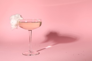 Photo of Tasty cocktail in glass decorated with cotton candy on pink background, space for text