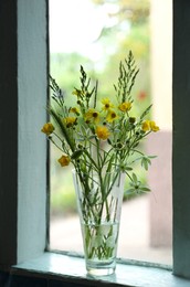 Bouquet of beautiful wildflowers in glass vase on window sill indoors