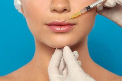 Young woman getting lips injection on color background, closeup. Cosmetic surgery