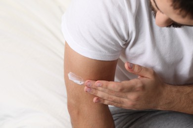 Man with dry skin applying cream onto his arm on bed, closeup