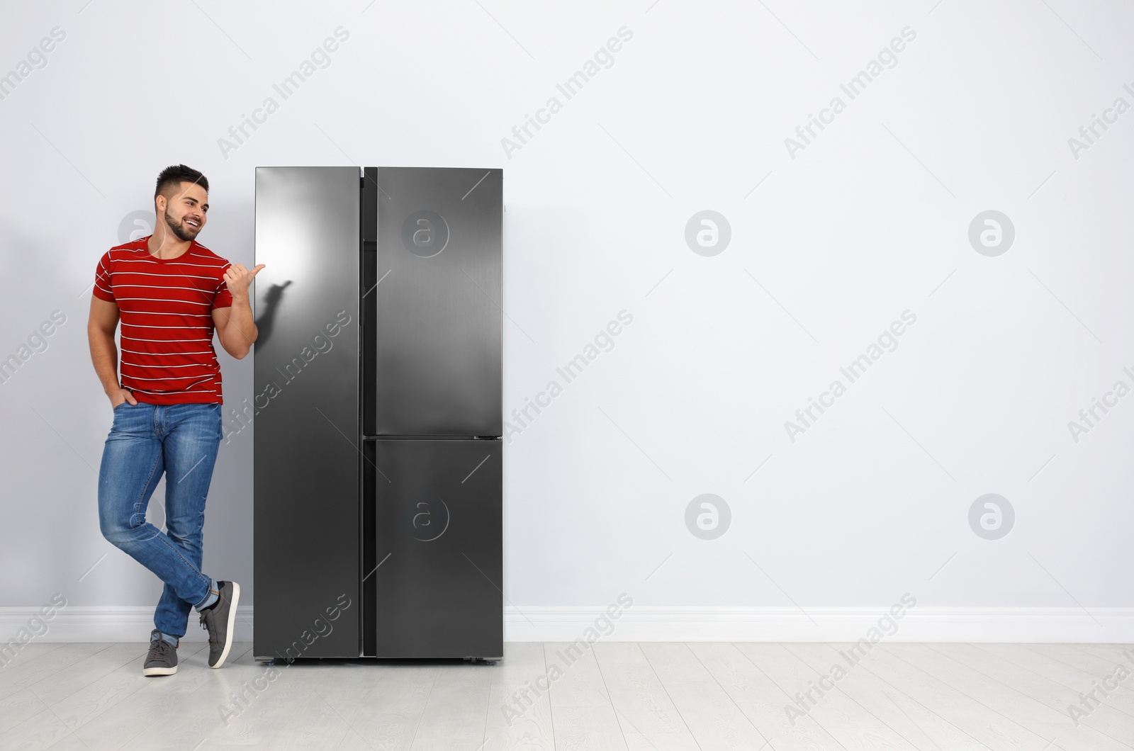 Photo of Happy young man near refrigerator indoors, space for text