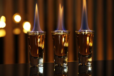 Flaming alcohol drink in shot glasses on mirror surface against blurred background