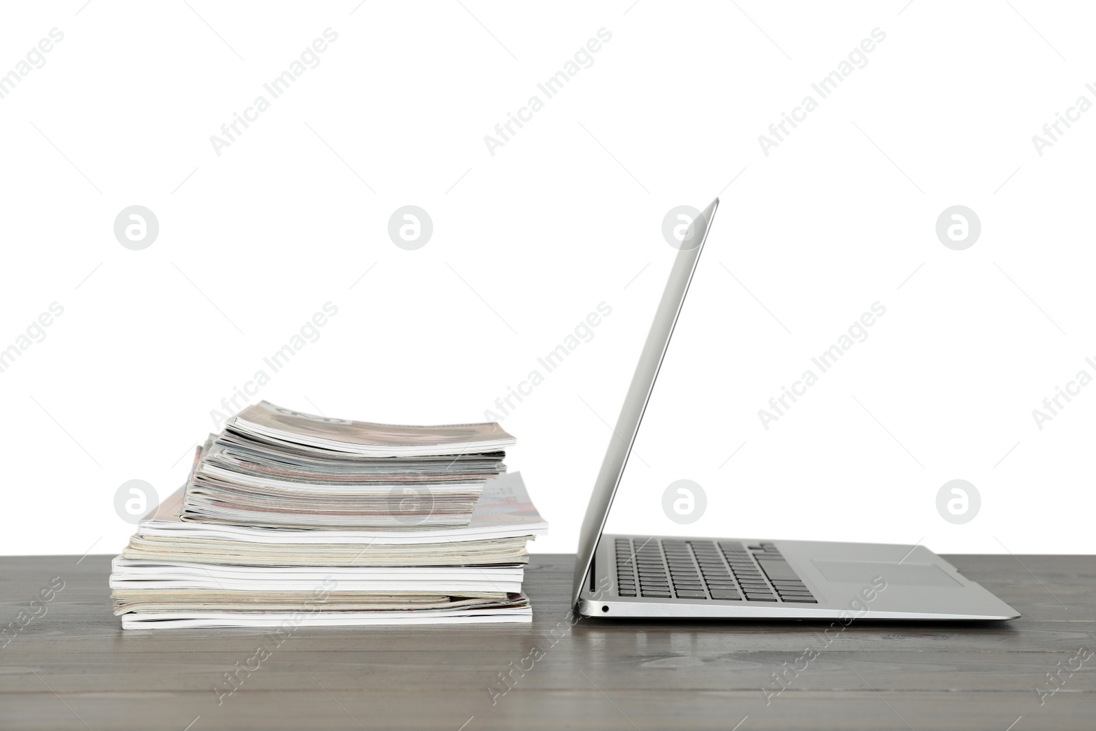 Photo of Stack of magazines and laptop on table near white wall