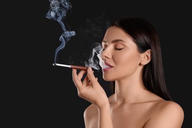 Woman using long cigarette holder for smoking on black background, space for text