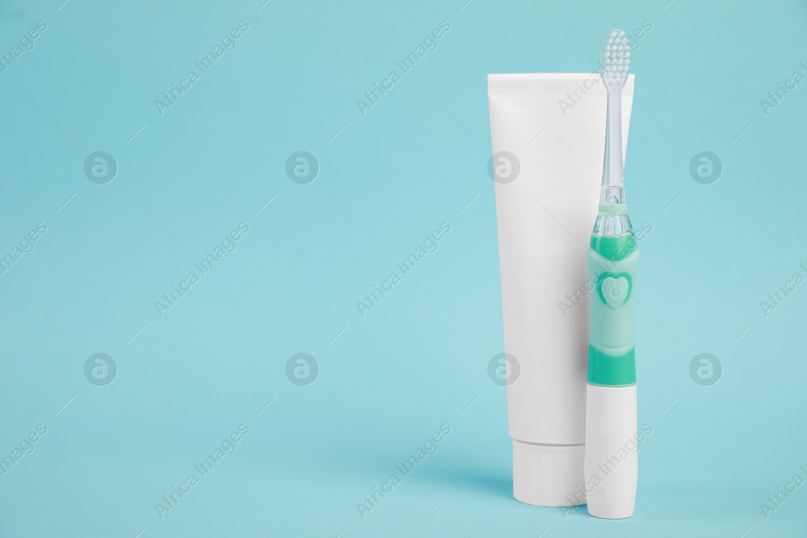 Photo of Electric toothbrush and toothpaste on light blue background, space for text