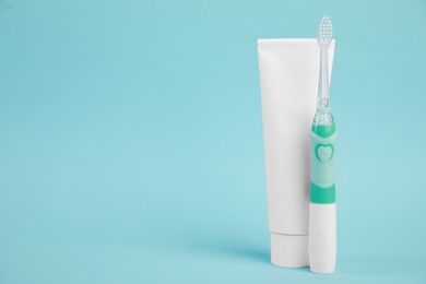 Photo of Electric toothbrush and toothpaste on light blue background, space for text
