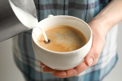 Photo of Woman pouring milk into cup of hot coffee, closeup