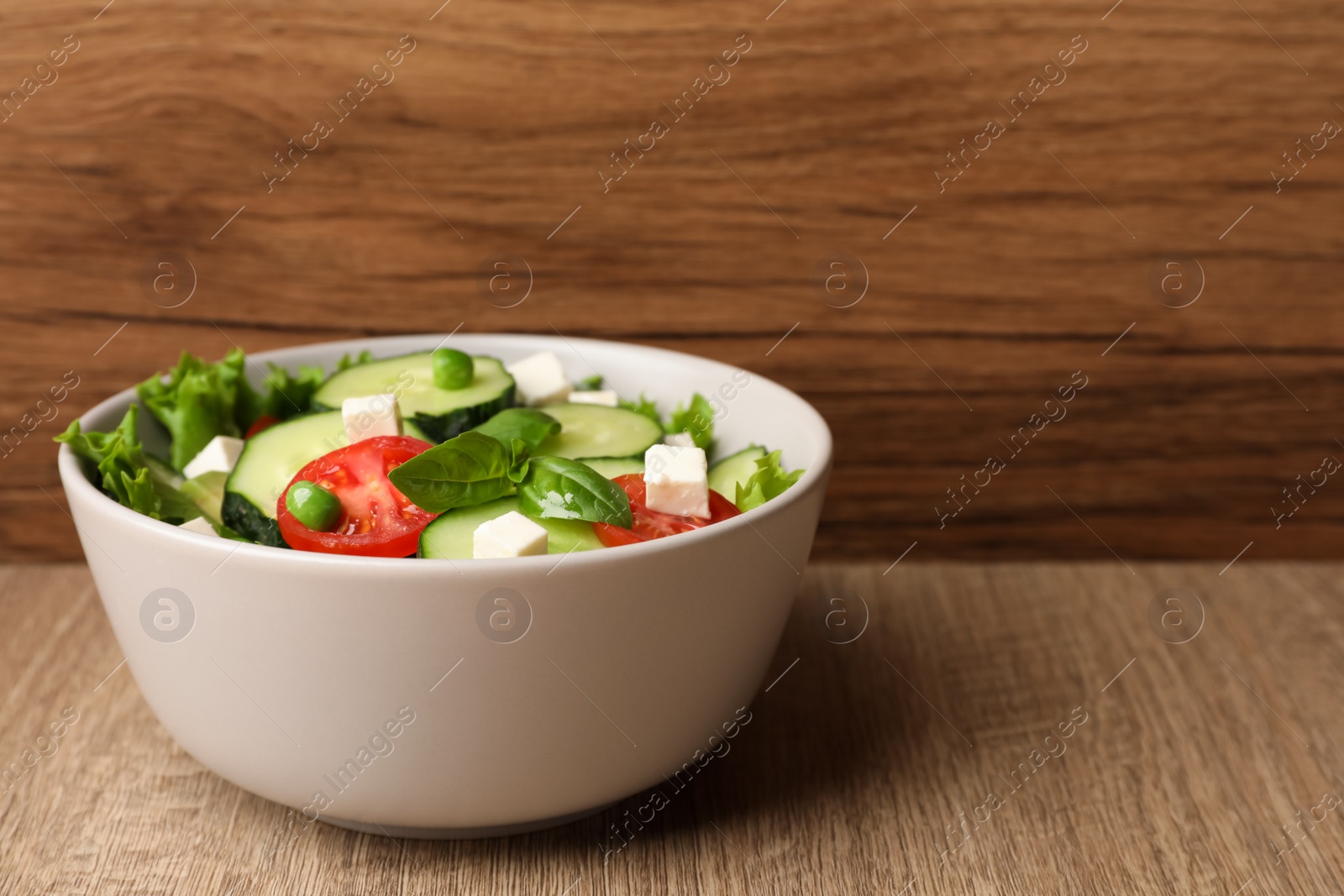 Photo of Tasty fresh salad with cucumber in bowl on wooden table, space for text