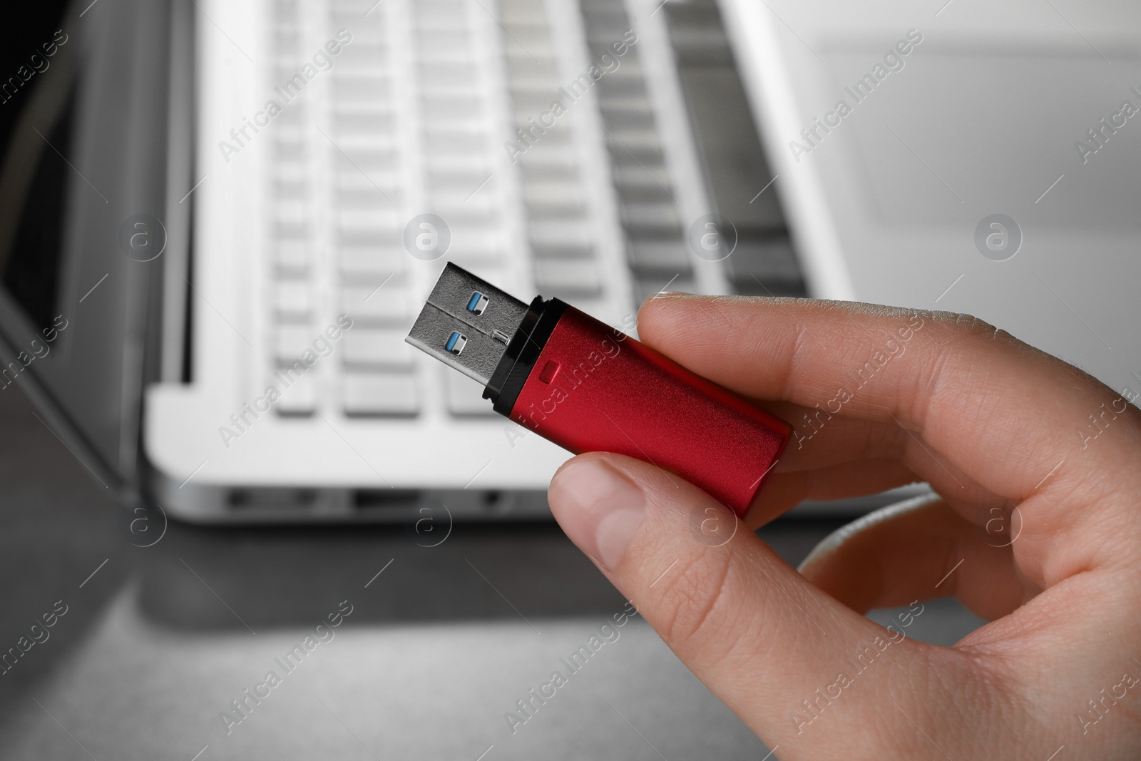 Photo of Woman holding usb flash drive near laptop, closeup