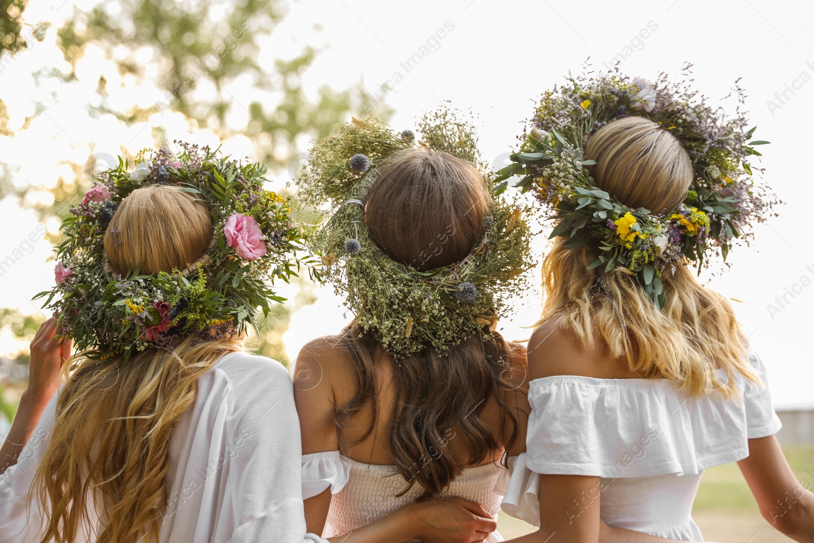 Photo of Young women wearing wreaths made of beautiful flowers outdoors on sunny day, back view