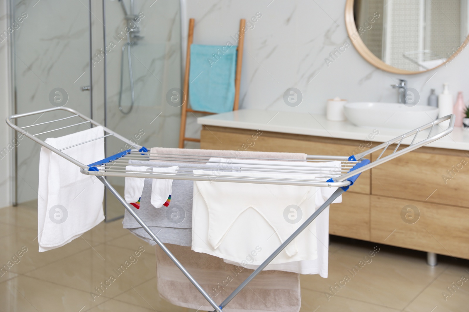 Photo of Clean laundry hanging on drying rack in bathroom