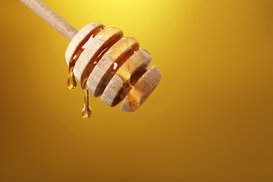 Photo of Delicious honey flowing down from dipper against golden background, closeup. Space for text