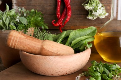 Photo of Mortar with pestle, fresh green herbs and oil on wooden table