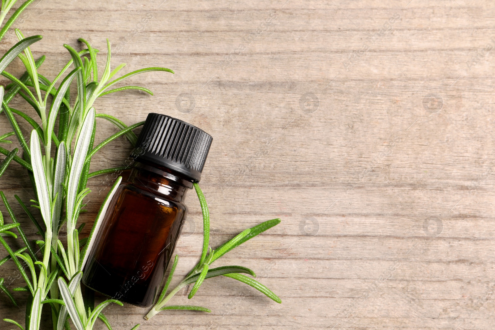 Photo of Bottle of essential oil and fresh rosemary sprigs on wooden table, flat lay. Space for text