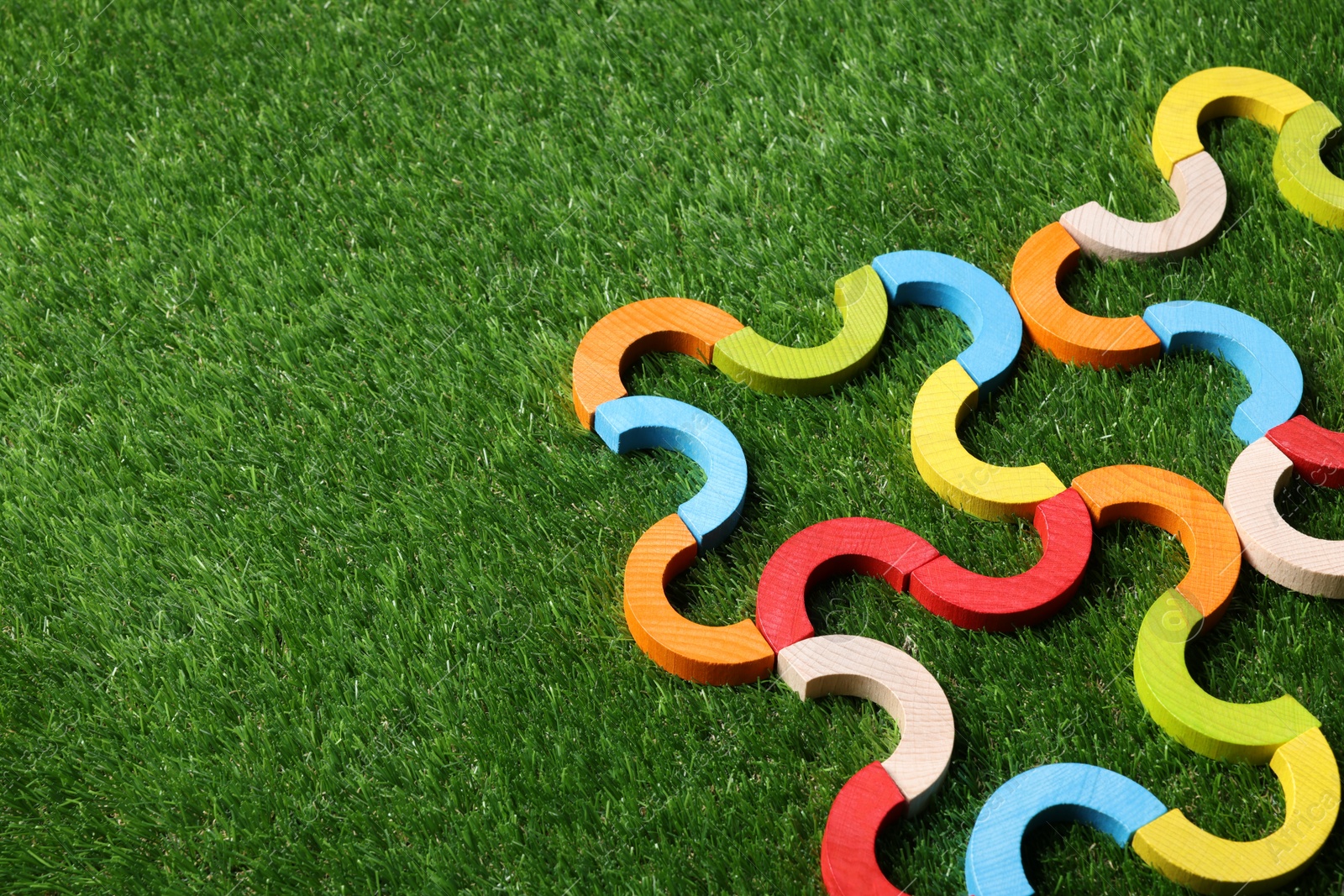 Photo of Colorful wooden pieces of play set on green grass, above view with space for text. Educational toy for motor skills development