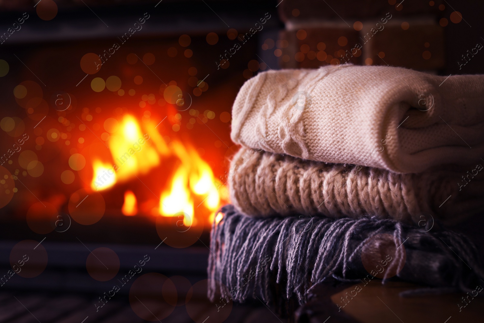 Image of Stack of knitwear near fireplace with burning wood indoors. Winter vacation