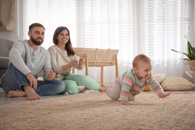 Photo of Happy parents watching their baby crawl on floor at home