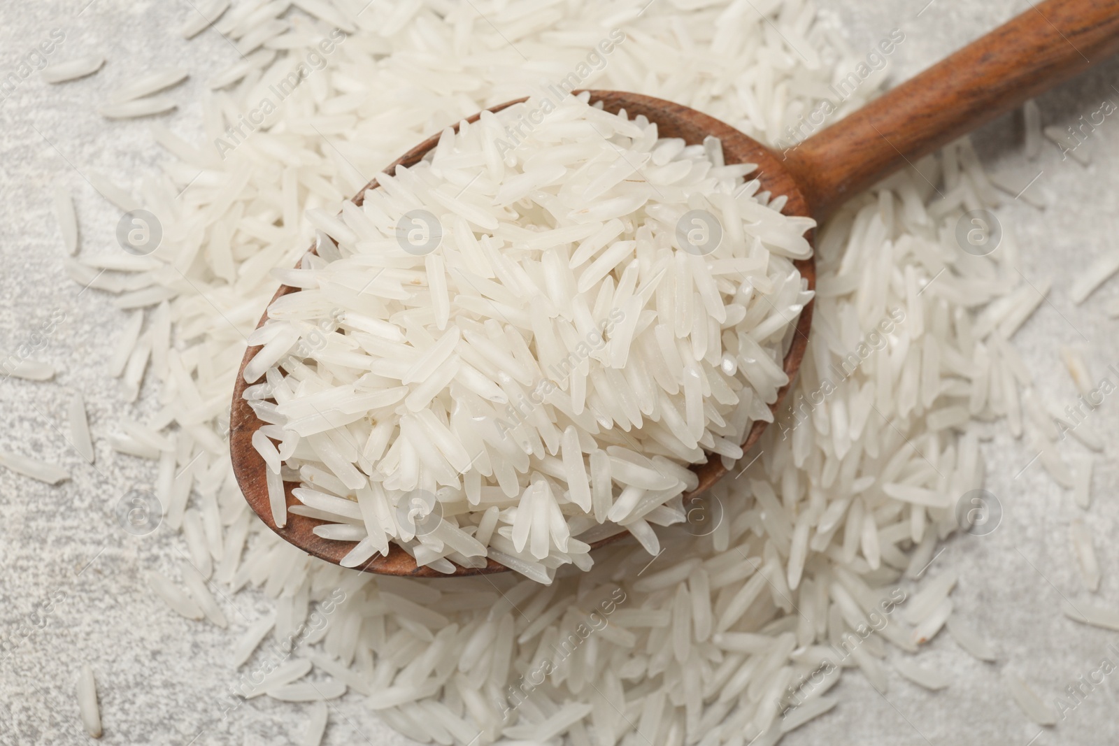 Photo of Raw basmati rice and wooden spoon on grey table, top view