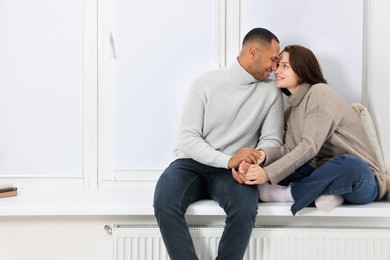 Photo of Dating agency. Happy couple holding hands and sitting on window sill at home, space for text