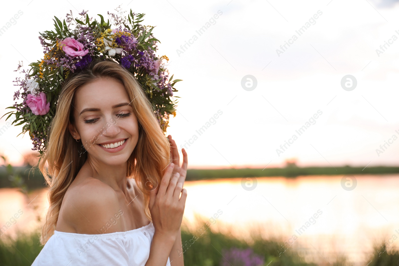 Photo of Young woman wearing wreath made of beautiful flowers outdoors at sunset