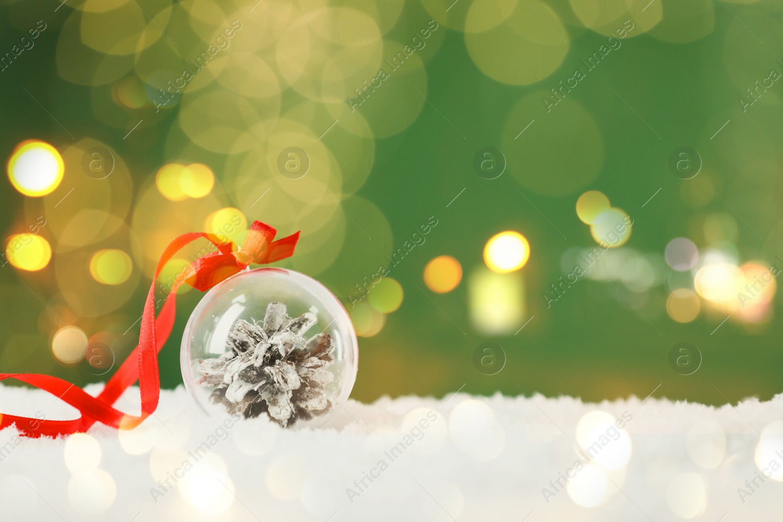 Image of Beautiful transparent Christmas ornament with fir cone on snow against green background, bokeh effect. Space for text