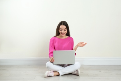 Photo of Young woman with laptop sitting on floor near light wall indoors