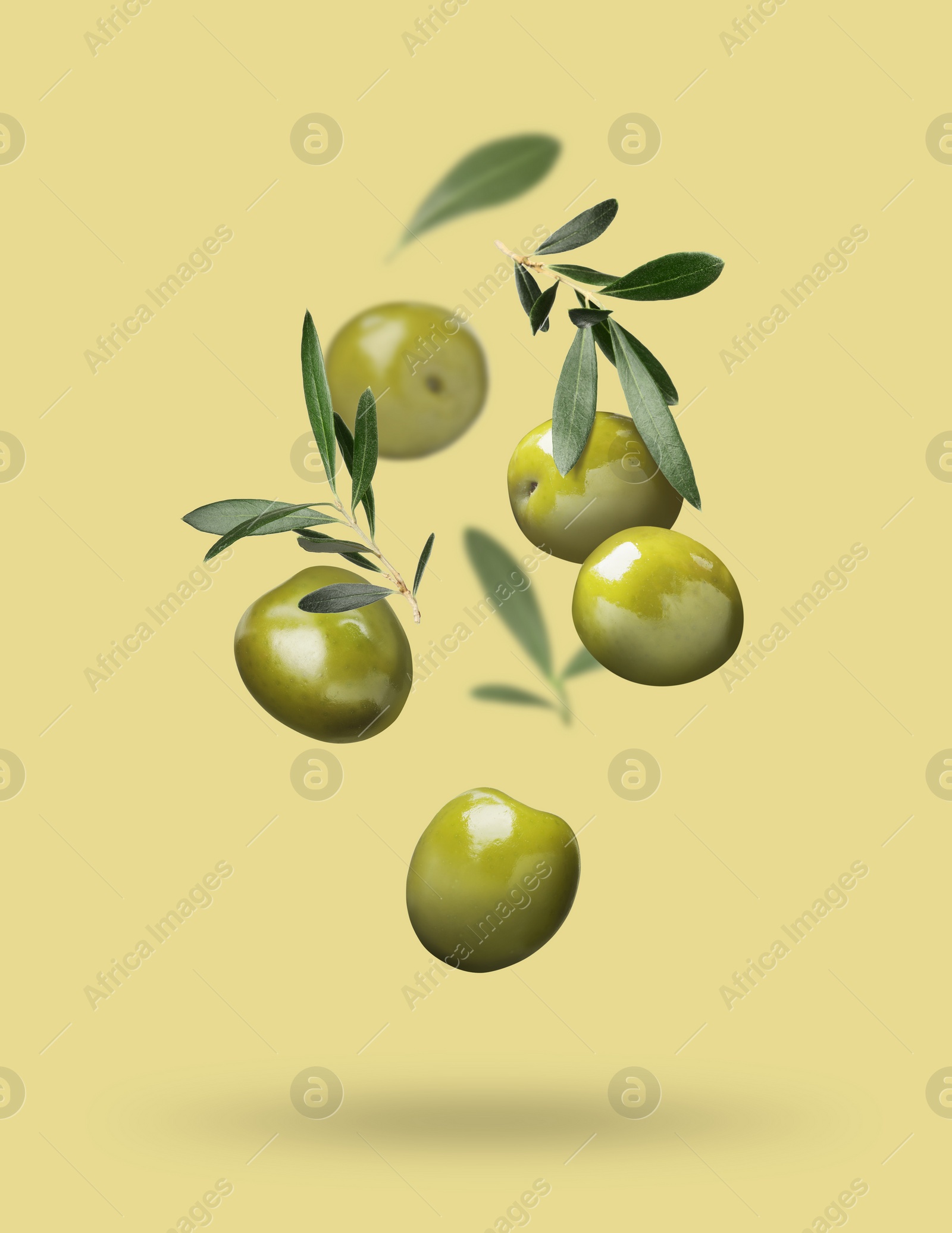 Image of Fresh olives and leaves falling on pale yellow background