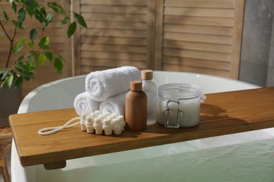 Photo of Wooden tray with spa products and towels on bath tub in bathroom