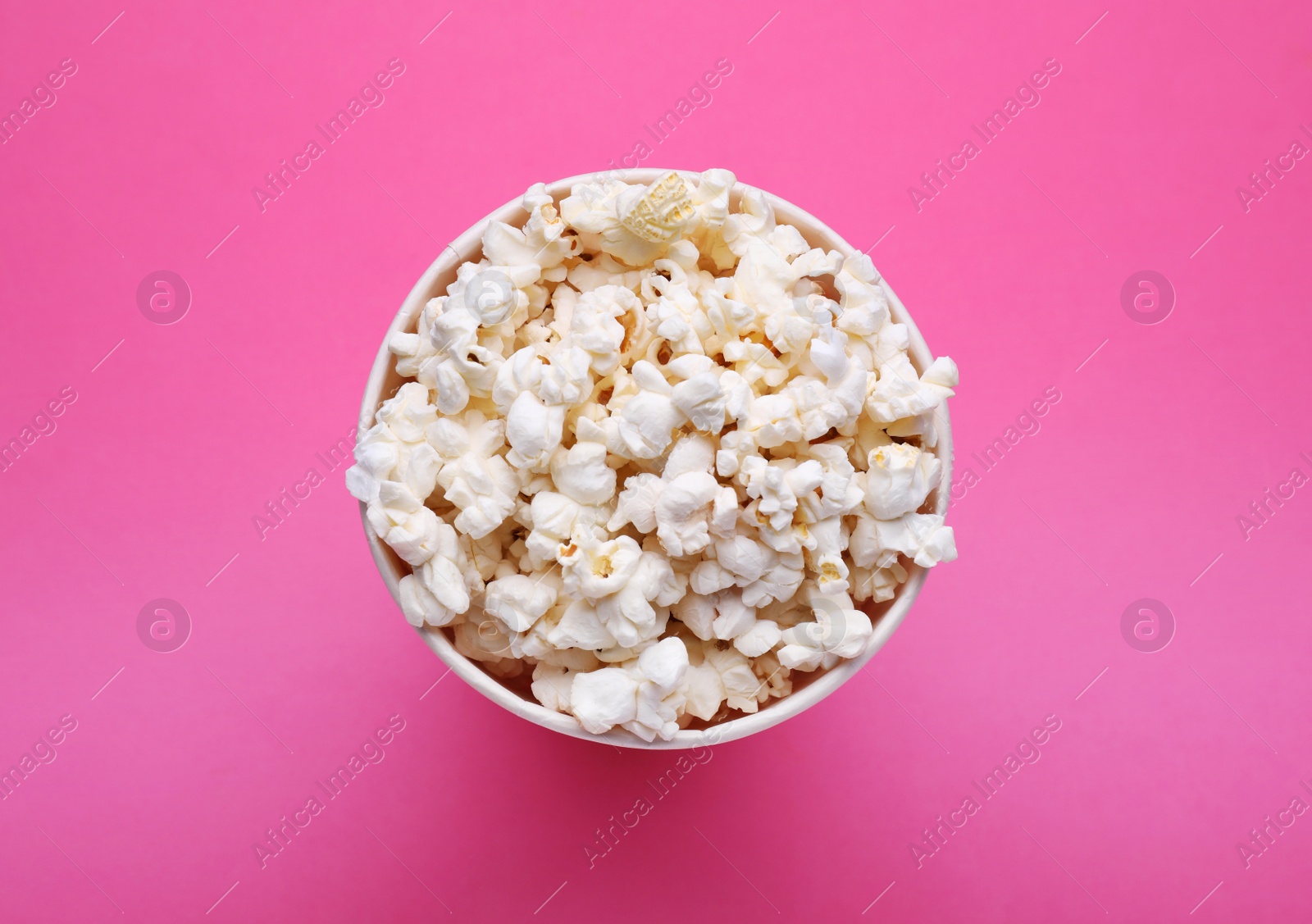 Photo of Paper bucket with delicious popcorn on pink background, top view