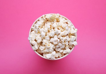 Photo of Paper bucket with delicious popcorn on pink background, top view