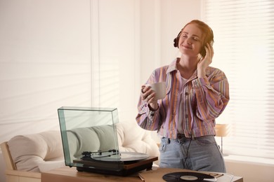 Photo of Young woman drinking coffee while listening to music with turntable in living room