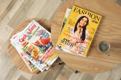 Wooden nesting tables with different magazines and cup of coffee indoors, top view