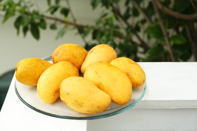 Photo of Delicious ripe yellow mangoes on glass plate outdoors