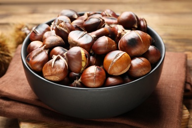 Photo of Delicious roasted edible chestnuts in bowl on table, closeup