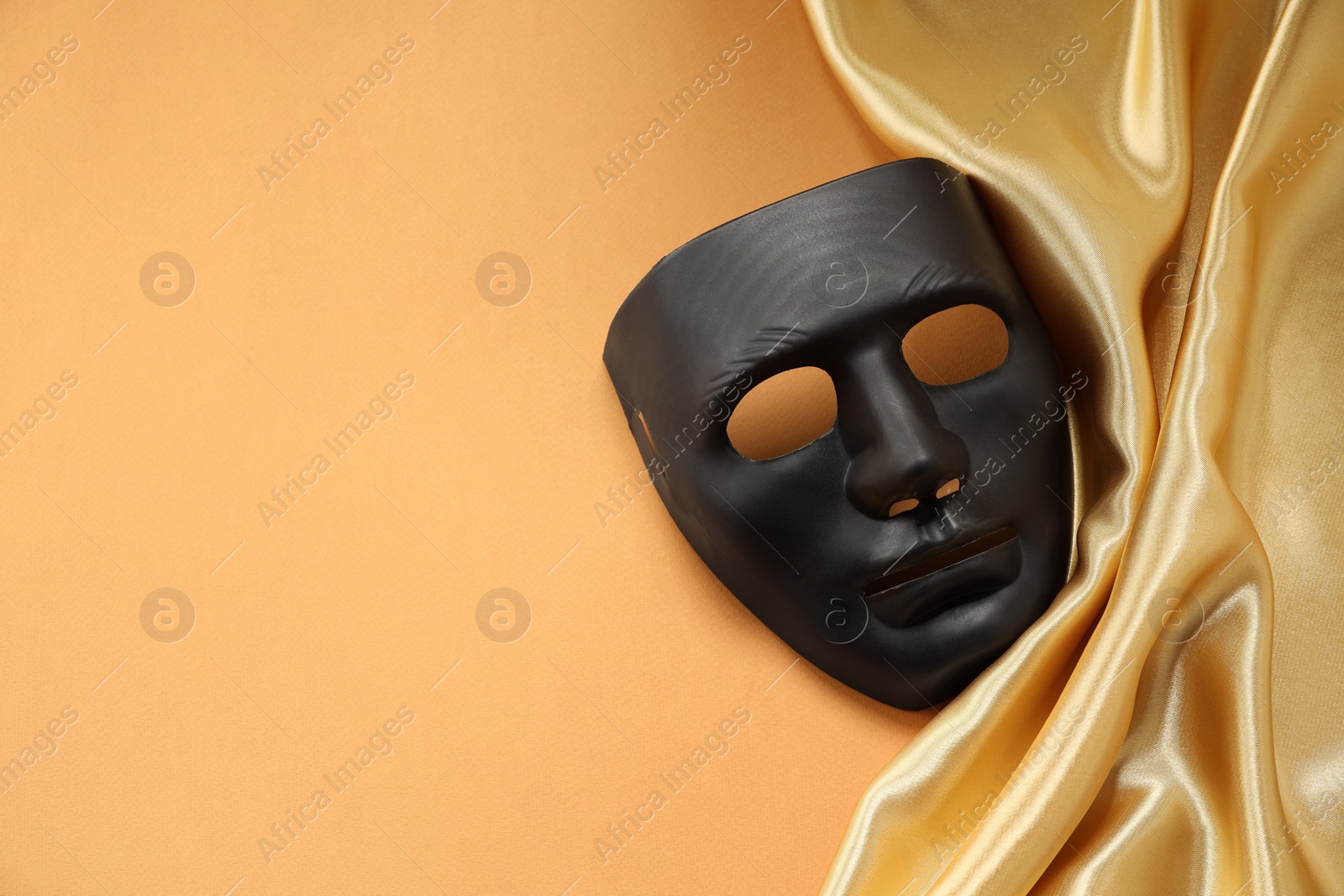 Photo of Theater arts. Black mask and golden fabric on pale orange background, top view. Space for text