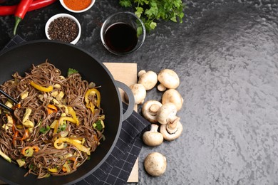 Photo of Stir-fry. Tasty noodles with meat and vegetables in wok served on dark textured table, flat lay. Space for text