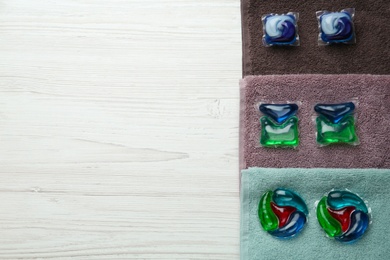 Laundry capsules and towels on white wooden table, flat lay. space for text