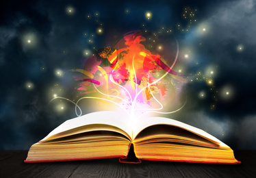 Image of Open book with fairytales and magic lights on wooden table. Creative design