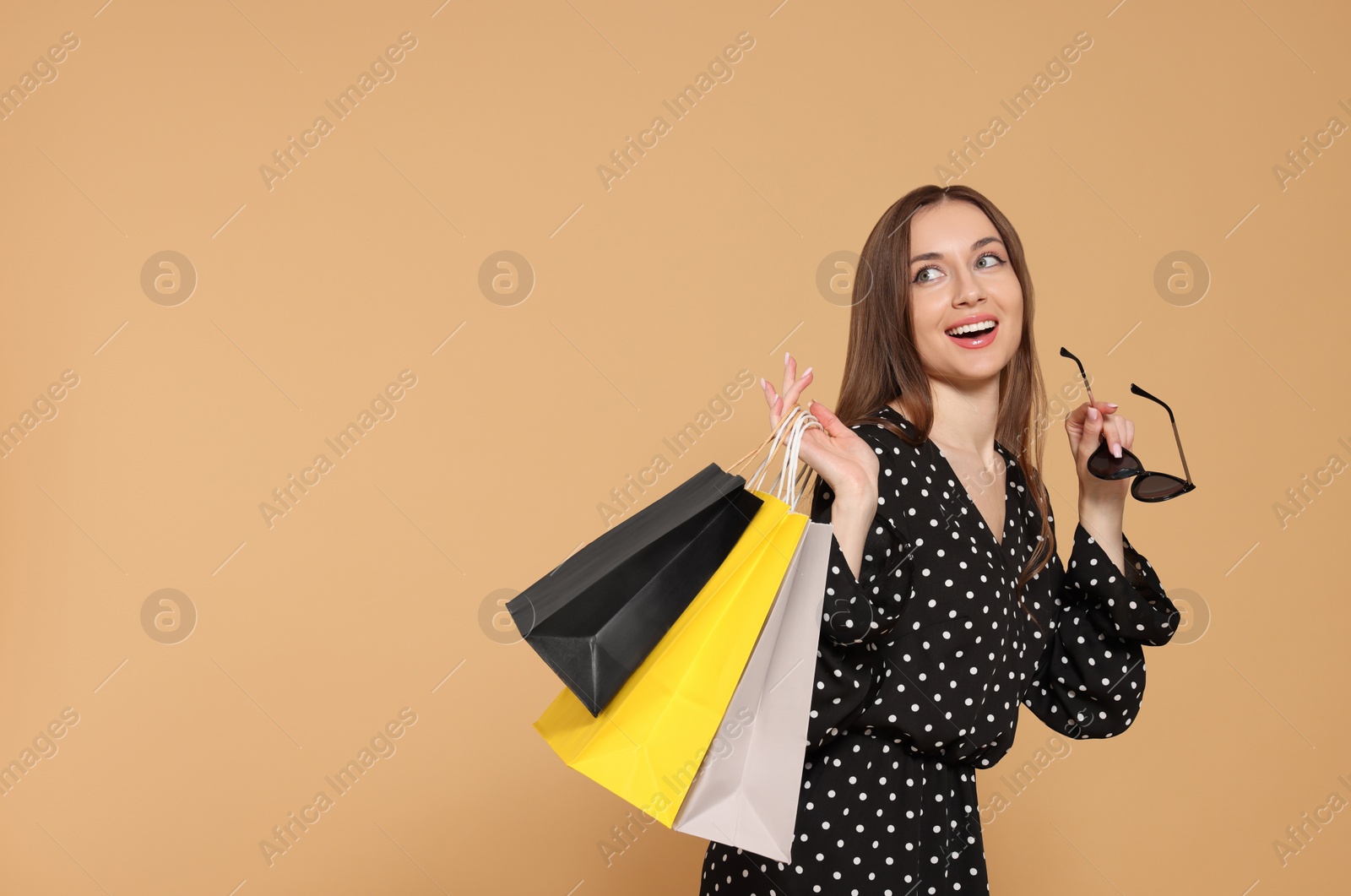 Photo of Stylish young woman with sunglasses and shopping bags on beige background, space for text