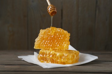 Photo of Dripping tasty honey from dipper onto honeycombs on wooden table