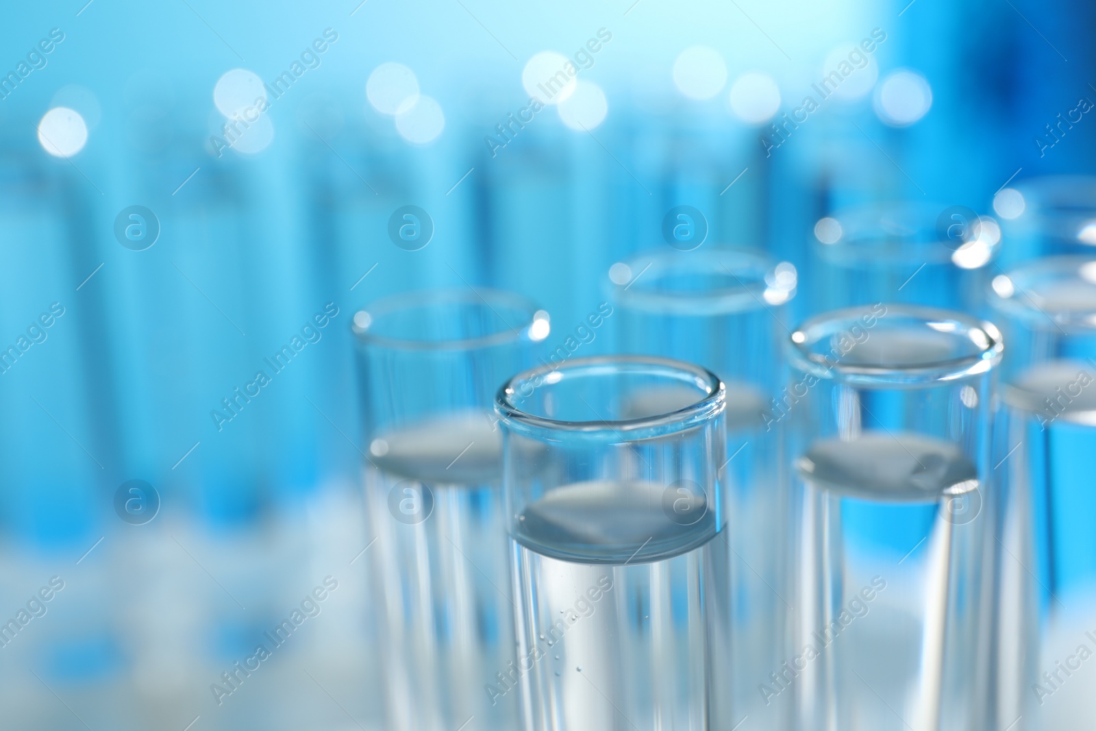 Photo of Many glass test tubes on light blue background, closeup