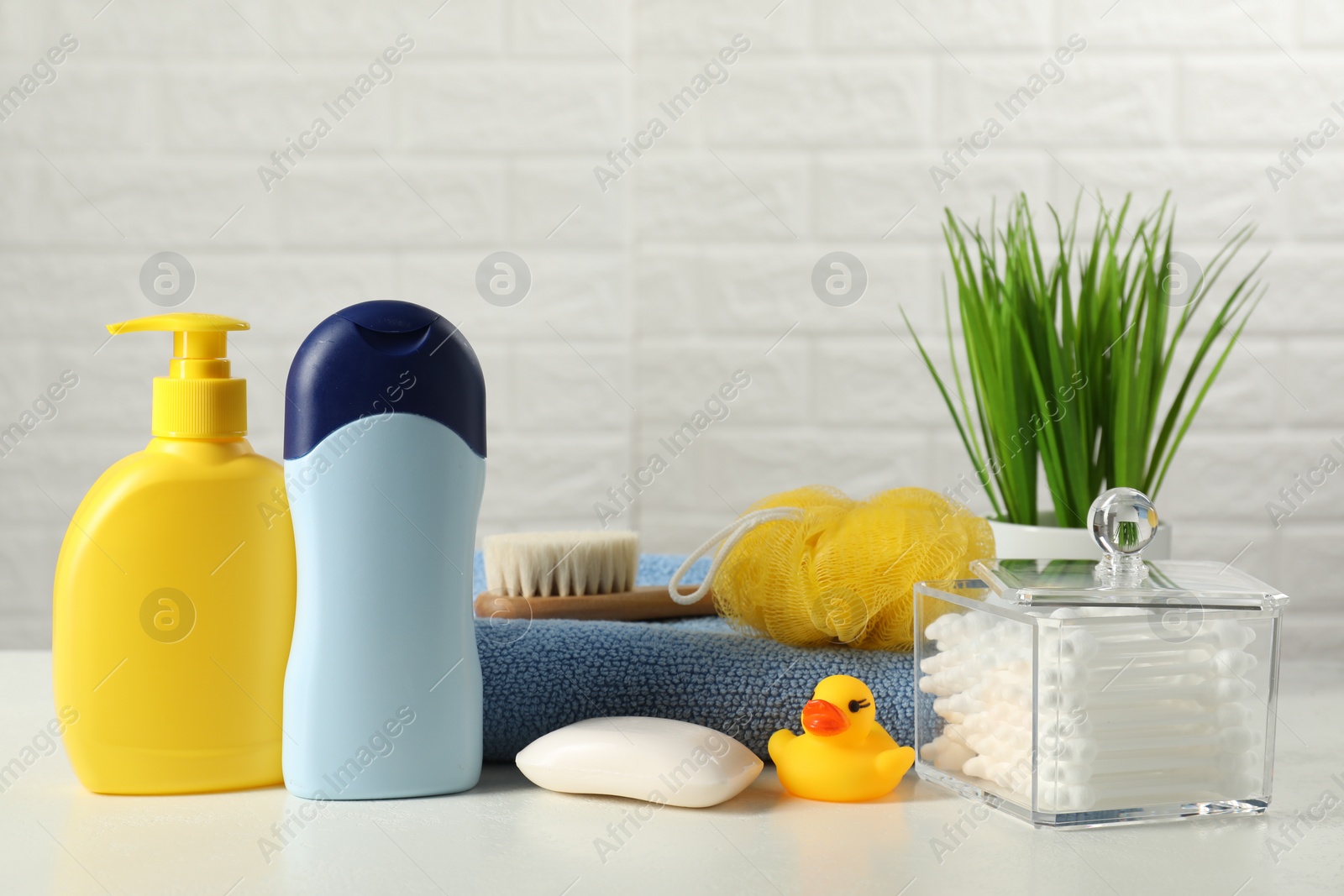 Photo of Baby cosmetic products, bath duck, brush and towel on white table against brick wall