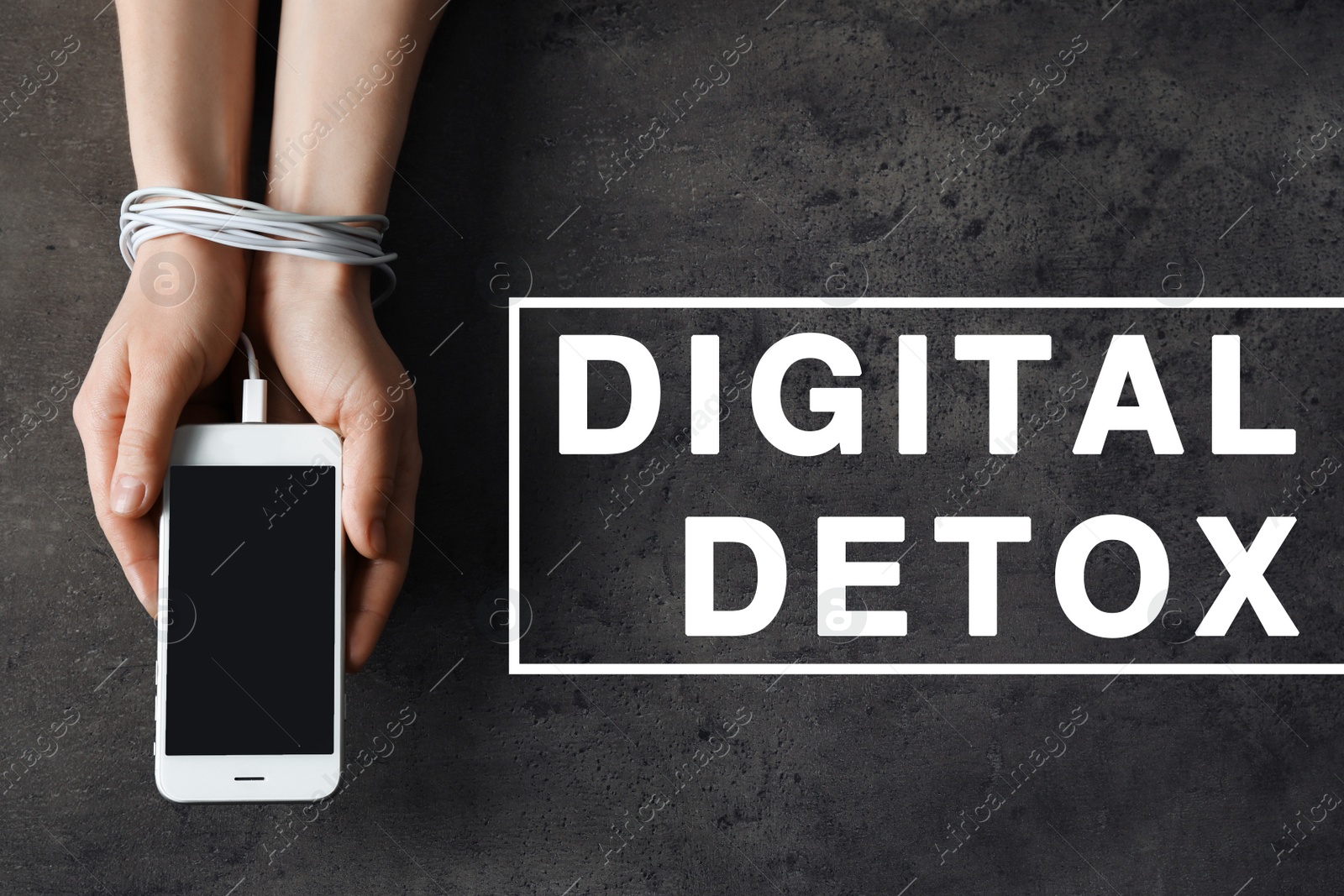 Image of Digital detox concept. Woman holding mobile phone in hands tied with charging cable near text on grey background, above view